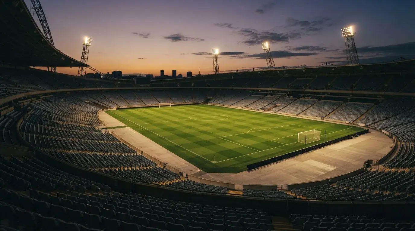 An empty football stadium with floodlight masts at dusk